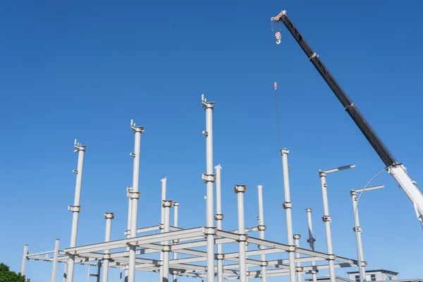 青い空の下で新しい建物のための構造鋼フレーミング上に高くそびえる建設クレーン — ストック写真