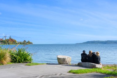 Taupo Yeni Zelanda - 16 Nisan 2023; Gölün kenarında oturan üç genç yetişkin.