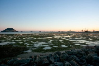 Tauranga Limanı boyunca uzanan Maunganui Dağı uzak ufuktaki gelgitte gün doğumunda