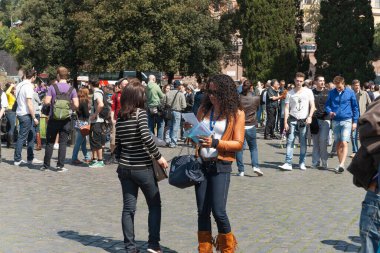 Roma İtalya - 16 Nisan 2011; İki modern trend genç kadın caddenin ortasında seyahat belgelerine bakarken kalabalık geçip gidiyor.
