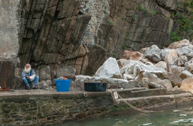 Riomaggiore İtalya - 23 Nisan 2011; büyük beyaz sakallı son sınıf öğrencisi kaya yüzeyinin dibinde oturmuş gazete okuyordu.