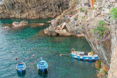 Riomaggiore İtalya - 26 Nisan 2011; Tipik Avrupa tekneleri aşağıda Riomaggiore Körfezi 'nde güneşlenen ve çevresindeki kayalıklar üzerinde dinlenen genç yetişkinler.