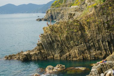 Riomaggiore İtalya 26 Nisan 2011; Güneş banyosu yapanlar okyanusa düşen engebeli dikey desenli yüksek kayalıklardan atlayan ve dalan gençleri izliyorlar.