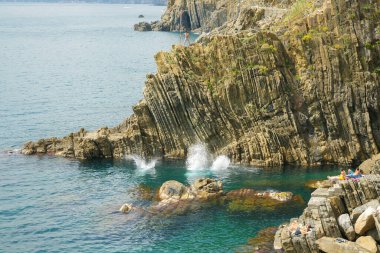 Riomaggiore İtalya 26 Nisan 2011; Güneş banyosu yapanlar okyanusa düşen engebeli dikey desenli yüksek kayalıklardan atlayan ve dalan gençleri izliyorlar.