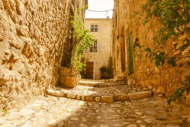 Taş duvarlar arasında dar bir yerleşim yeri. Tipik bir Akdeniz sahnesinde geçitlerden geçiyor. Saint Paul de Vence, Provence, Fransa.