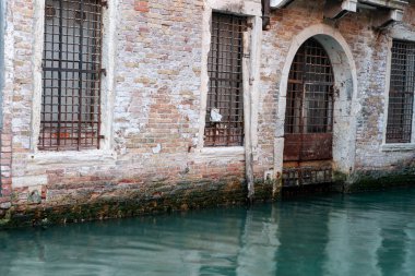 Venice Italy - May 10 2011; Old brick building with security protected window and door alongside and reflected in green water of canal.