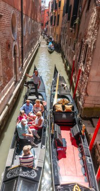 Venice Italy - May 10 2011; Tourists being carried on gondola between high walls of buildings lining narrow canal.