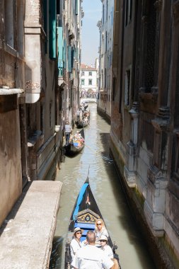 Venice Italy - May 10 2011; Tourists being carried on gondola between high walls of buildings lining narrow canal.