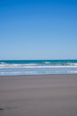 Opunake sörf plajı batı kıyısı siyah kum, mavi gökyüzü ve su.