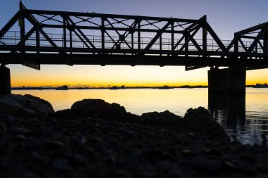 Rocky liman kenarları ve tren yolu gelini güneş doğmadan önce arka planda. Tauranga Limanında..