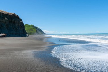Siyah kumsalda ve dik kayalıklarda dalgalanan beyaz su Yeni Zelanda.