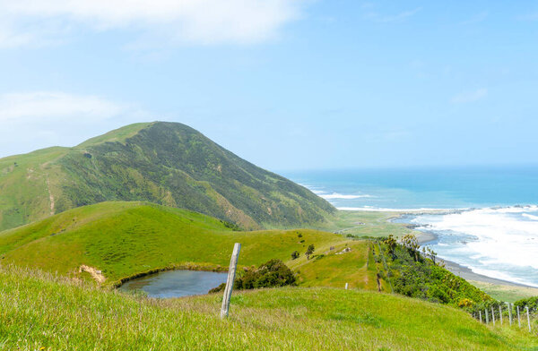 Холмистые сельхозугодия с прудом и видом на побережье Вайрарарапы и серфинг под голубым небом