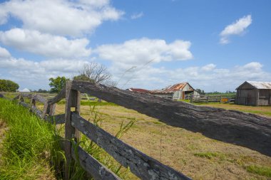 Eski yıpranmış demiryolu ve demiryolu çitleri arka planda eski kıvrımlı demir çiftlik kulübeleriyle otoyol boyunca uzanıyor. Ulmarra ve Yamba arasındaki kırsal bölgeler.