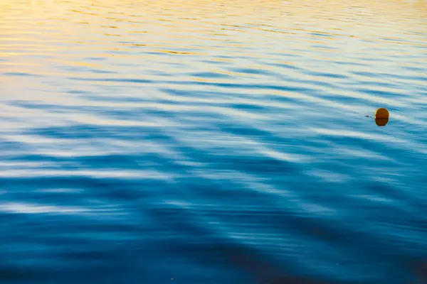 stock image Gold and blue rippled water surface with orange colour buoy.