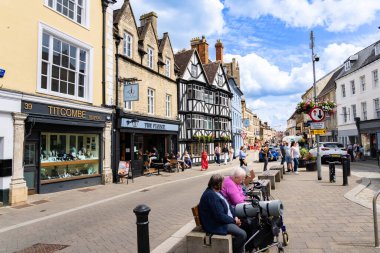 Cirencester United Kingdom - July 26 2024; Downtown city street with people and variety building facades and gables. clipart