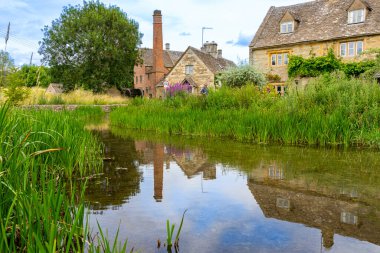 Eski tuğla kule ve taş binalar, Aşağı Katliam 'daki yeşil bitki örtüsünün oluşturduğu sakin nehre yansıyor..