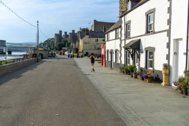 Conwy Wales - 30 Temmuz 2024; Aşağı Kapı Caddesi 'ndeki en küçük Galler ve beyaz binaların önünden geçen kadın.