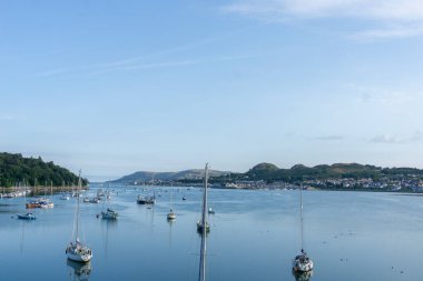 Conwy nehri boyunca rıhtımdaki teknelere ve temiz mavi gökyüzüyle nehre demirlenmiş nehirlere bakın..