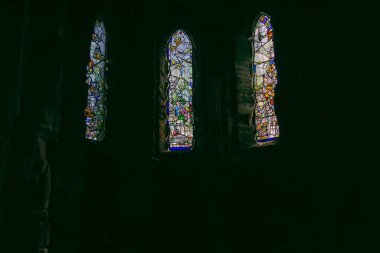 Arka planda taş duvara yerleştirilmiş dini vitray pencereler var..