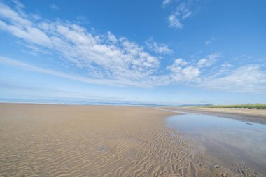 Manzaralı Harlech Sahili kumulları, çimenler ve kumdaki dalgalanma desenleri mavi gökyüzünün altında ve kuzey Galler 'deki yüksek rüzgarlı beyaz bulutlar altında..