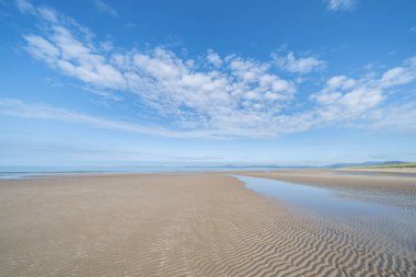 Manzaralı Harlech Sahili kumulları, çimenler ve kumdaki dalgalanma desenleri mavi gökyüzünün altında ve kuzey Galler 'deki yüksek rüzgarlı beyaz bulutlar altında..