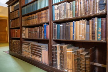 Lacock United Kingdom - August 9 2024; Bookcase loaded with ancient books bound in traditional style.. clipart