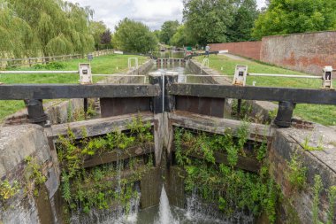 Birleşik Krallık - 10 Ağustos 2024; Kennet ve Avon Kanalı 'ndaki yeşil bitki örtüsü ile kaplı ikiz kapılardan geçen kilitler ve botlar.