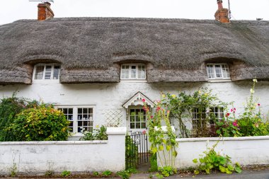 Tipik büyük, eski İngiliz bungalovu tarzı ev. Su sazlıklarından yapılmış sazlı çatı ve kırsal sokaktan çitlerin üzerinde büyüyen çiçekleri olan İngiliz bahçesi..