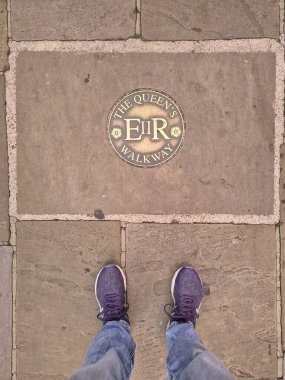 Queens Walkway 'de kot pantolon ve yürüyüş ayakkabısı giymiş turist bacakları. İngiltere Windsor' da pirinç kaplama plaketi..