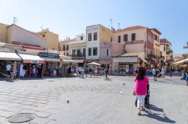 Chania Girit - 15 Ağustos 2024; PI yakınlarındaki turist dükkanları ve kafelerle çevrili büyük asfalt meydandaki insanlar. El. Venizelou.