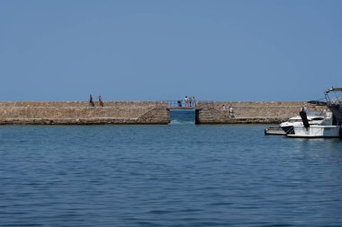 Chania - Girit - 17 Ağustos 2024; Akdeniz 'deki güzel bir günde liman boyunca dalgakıran yürüyüşü yapan insanlar.