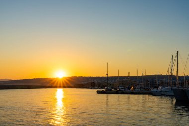 Güneş, Chania körfezinde batıyor. Binaların ve teknelerin üzerinde gölgeler var. Güneş ışığı ve mercek farkıyla arkadan aydınlatılan gölgeler olağanüstü bir arka plan oluşturuyor Girit..