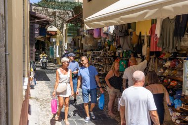 Rodos Yunanistan - 19 Ağustos 2024; Alışveriş torbaları taşıyan ve yürüyüş yapan çiftlerin bulunduğu turist dükkanları dar yol.