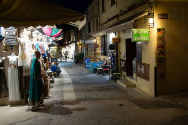 Rhodes, Yunanistan - 20 Ağustos 2024; Rhodes Old Town 'da gece vakti sokak tezgahları aydınlatıldı gölgelerde yaşayan insanlar ve loş sokak manzaraları aydınlatıldı.