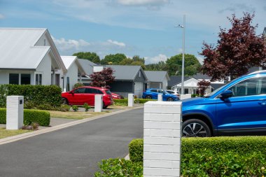 Garaj yollarında parlak kırmızı ve mavi arabaları olan modern alçak evlerin oturduğu cadde.