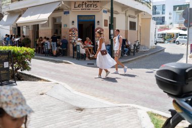 Kos Yunanistan - 21 Ağustos 2024; Lefteris restoranının önünde beyaz giyen akıllı genç çift caddede yürüyor.
