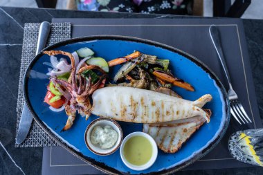 Yunan restoranındaki mavi tabakta soslu ızgara kalamar yemeği ve salata kuşbakışı..