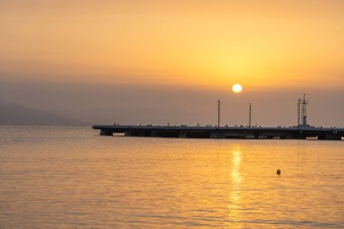 Koyda gün batımları Yunan adasında sakin su üzerinde altın bir parıltı sunuyor.