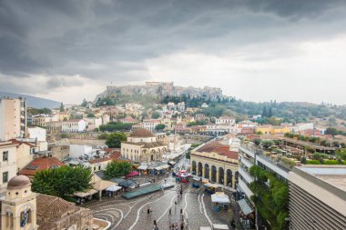 Atina - 30 Ağustos 2024; Monastiraki Meydanı Mahallesi 'nde Monastiraki Meydanı, aşağıdaki sokak ve binaları ve Akropolis' i kara bulutlar altında tepede görmek.