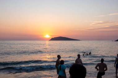 Kalymnos Yunanistan - 27 Ağustos 2024; Deniz aşırı güzel Akdeniz günbatımı sahnesinde tatilciler ve ada silueti.