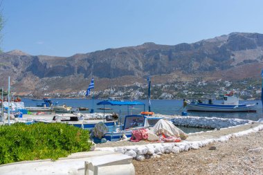 Telendos Yunanistan - 29 Ağustos 2024; Telendos Adası 'ndaki rıhtım sahnesi ve arka planda geleneksel balıkçı tekneleri ve ada tepeleri,