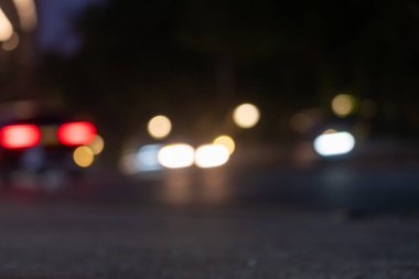 Şehir caddesinde hareket halindeki araçların kırmızı, mavi ve beyaz ışıkları koyu arkaplanda.