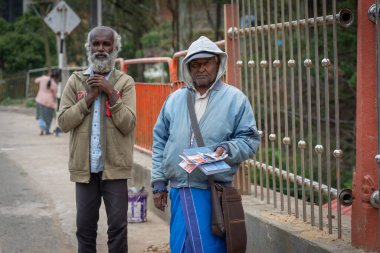 Sri Lanka - 7 Eylül 2024; Hindu Tapınağı 'nın yanındaki kaldırımda bir yaşlı adama bir kumarhane bileti satan iki adam.