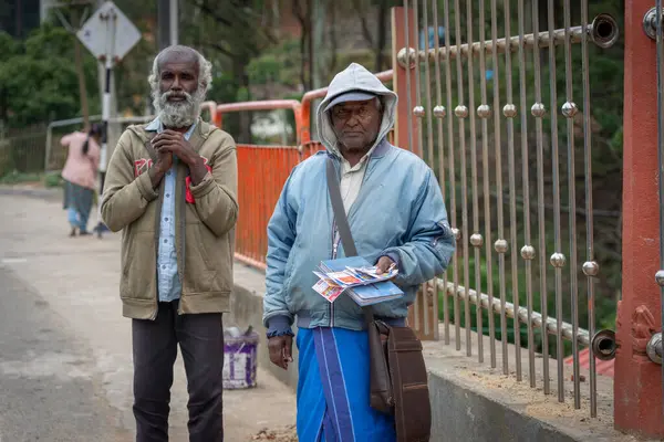 Sri Lanka - 7 Eylül 2024; Hindu Tapınağı 'nın yanındaki kaldırımda bir yaşlı adama bir kumarhane bileti satan iki adam.