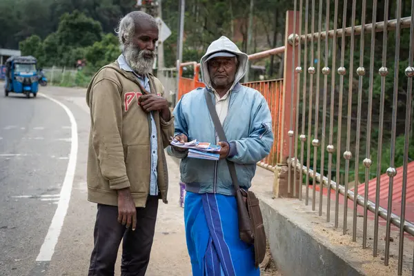 Sri Lanka - 7 Eylül 2024; Hindu Tapınağı 'nın yanındaki kaldırımda bir yaşlı adama bir kumarhane bileti satan iki adam.