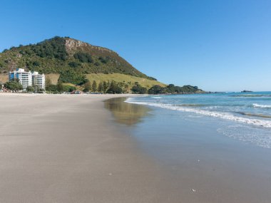 Maunganui Dağı, mavi gökyüzünün altında, uzun kumlu plajın sonunda Yeni Zelanda 'da..