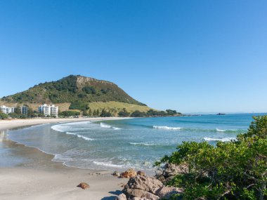 Maunganui Dağı, mavi gökyüzünün altında, uzun kumlu plajın sonunda Yeni Zelanda 'da..