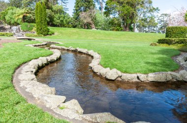 Taştan kenarlı akarsu, bahçe arazisinden Yatton Park Tauranga 'daki şelaleye doğru esiyor..
