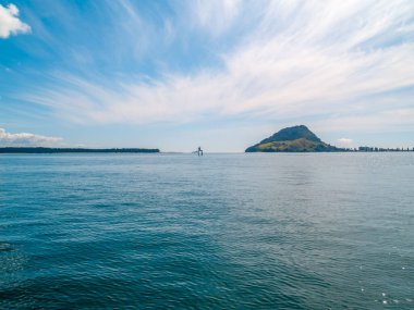 Tauranga limanından, ufuktaki Maunganui Dağı 'na beyaz bulut desenli, Yeni Zelanda' ya bakın..