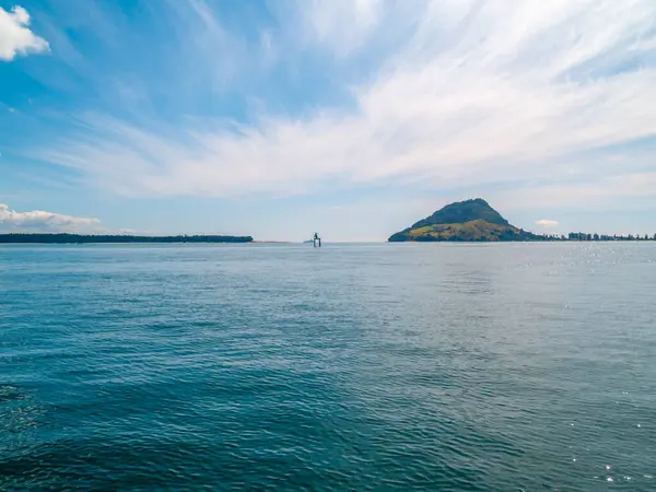 Tauranga limanından, ufuktaki Maunganui Dağı 'na beyaz bulut desenli, Yeni Zelanda' ya bakın..